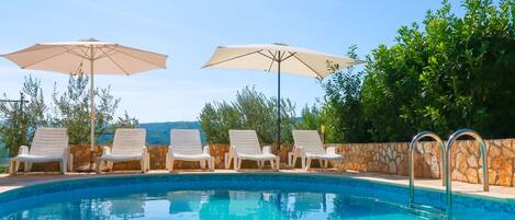 Une piscine entourée de murs de pierre et de verdure, avec des chaises longues et des parasols.