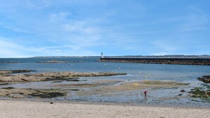 Un paysage côtier avec des rivages rocheux, un phare à l’horizon et un ciel dégagé.