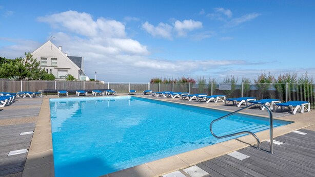 Une piscine entourée de chaises longues bleues et d’une terrasse en bois.