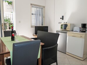 Eine kleine Küchenzeile mit Mikrowelle, Toaster und Kaffeemaschine. Ein Esstisch mit Stühlen und eine Flasche Wein sind vorhanden.