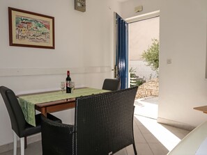 Un coin repas comprenant une table, des chaises, un tableau et une vue sur l’extérieur, visible à travers une porte ouverte.