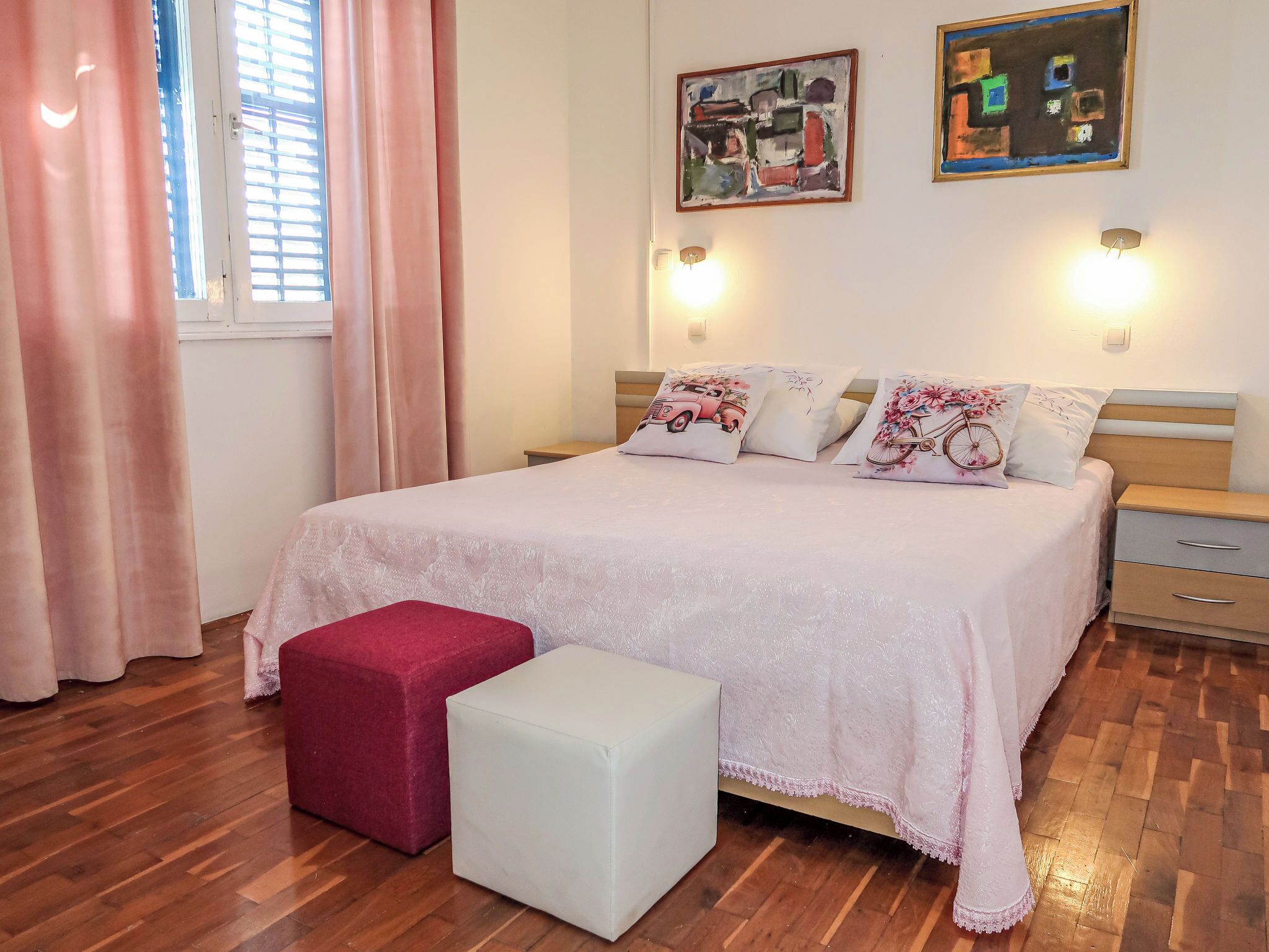 Une chambre à coucher comprenant un lit, deux tables de chevet, une commode, une fenêtre avec des rideaux et deux lampes fixées au mur.