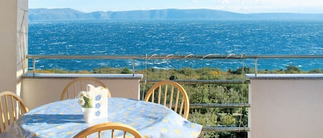 Un balcon avec une table et des chaises, donnant sur une mer où l’on aperçoit des montagnes au loin.