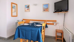 A dining area with a table set for four, a television mounted on the wall, and framed pictures on the wall. - Seaview - flat for 4 (Pornichet)