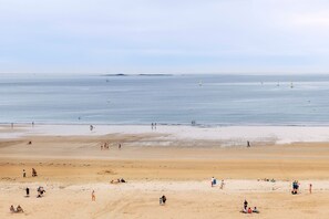 Ein weiter Sandstrand mit badenden und spazierenden Personen.