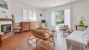 A spacious living room with a fireplace, wicker furniture, a television, and large windows. - Less than 2km from the beach, house for 6 (Andernos-les-Bains)
