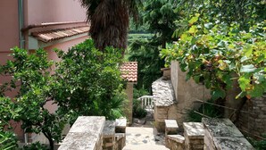 A stone staircase leading to a courtyard with a tiled floor, surrounded by lush greenery and a stone wall. - Vacation home Noel by Interhome (Labin)