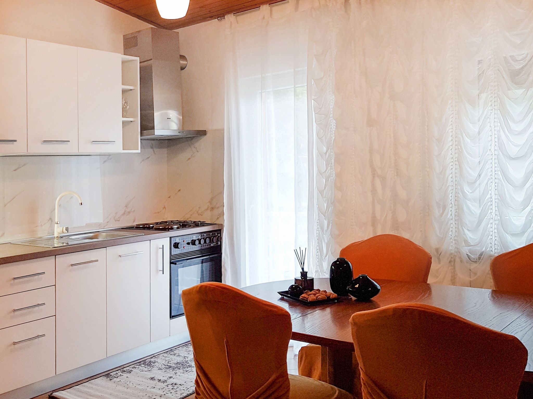 Une cuisine moderne avec des meubles blancs, une cuisinière à gaz et un coin repas doté de chaises orange.