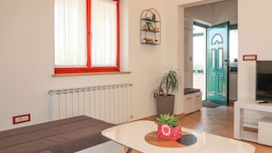 Een moderne woonkamer met een bank, een witte salontafel, een plant in pot en een televisie.