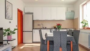 Een compacte keuken met witte kastjes, een inbouwoven en een eethoek met een tafel en stoelen.