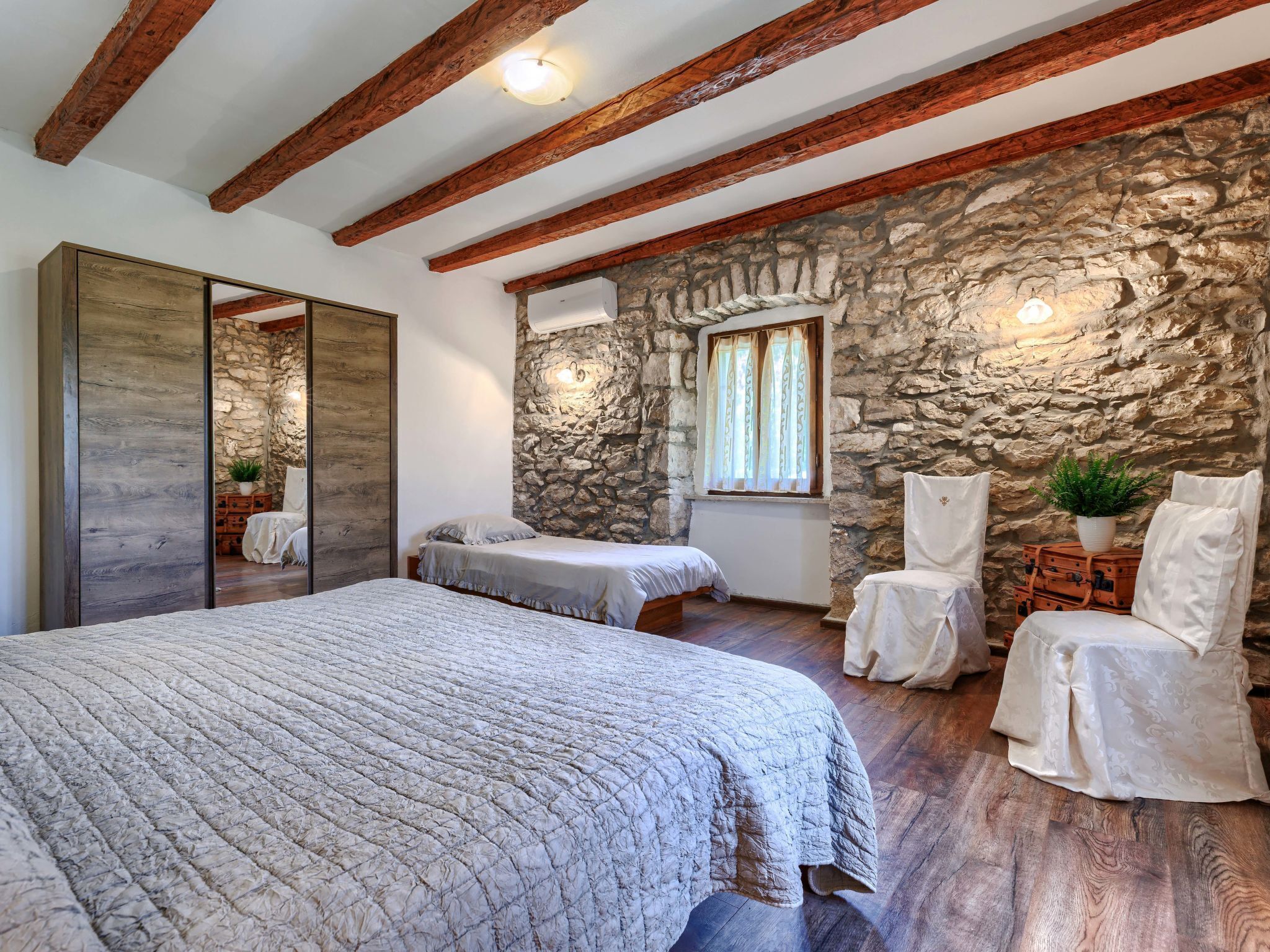 Una camera da letto con un letto grande, due letti più piccoli, pareti in pietra, travi di legno e un camino in pietra.
