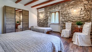 Ein Schlafzimmer mit einem großen Bett, zwei Einzelbetten, Steinwänden, Holzbalken und einem Kamin aus Stein.