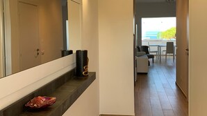 Un pasillo con suelo de madera, un banco empotrado con objetos decorativos, un espejo y vistas a un comedor con mesa y sillas.