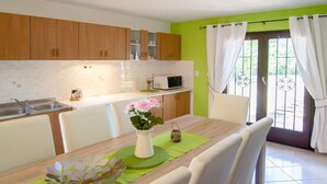 A modern kitchen with wooden cabinets, a dining table with chairs, a vase of flowers, and a view through a glass door. - Vacation home Sara by Interhome (Poreč)
