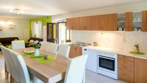A modern kitchen with wooden cabinets, a white stove, and a dining area with a wooden table and white chairs. - Vacation home Sara by Interhome (Poreč)