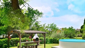 A gazebo with a table and bench, surrounded by lush greenery and a swimming pool. - Vacation home Sara by Interhome (Poreč)