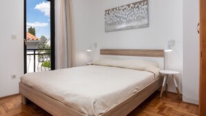 Ein Schlafzimmer mit einem hölzernen Bett, Blick durch ein Fenster, einem Bild an der Wand und einem kleinen Nachttisch mit einer Lampe.