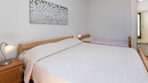 Ein Schlafzimmer mit einem großen Bett, einem kleineren Bett, einem Nachttisch mit Lampe und einem an der Wand hängenden Gemälde.
