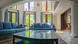 Un salon spacieux, doté d’un grand canapé, d’une table basse en verre et offrant une vue sur l’extérieur grâce à de grandes fenêtres.