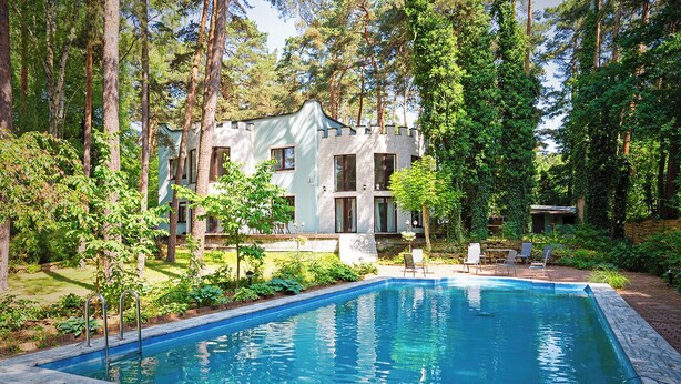 Une maison moderne avec une piscine, entourée d’arbres.
