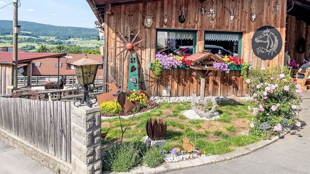 Ein rustikales Holzgebäude mit Windmühle, Blumenkästen und einer Pferdestatue.