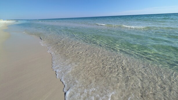 Una playa con aguas poco profundas y cristalinas, y una orilla arenosa.