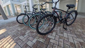 Una hilera de bicicletas estacionadas en un patio de ladrillo frente a un edificio con balcón y una puerta marcada con los números del 1 al 9.