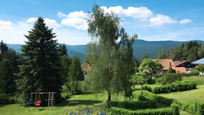 Un parque con un columpio, un árbol y una vista de casas y montañas al fondo.