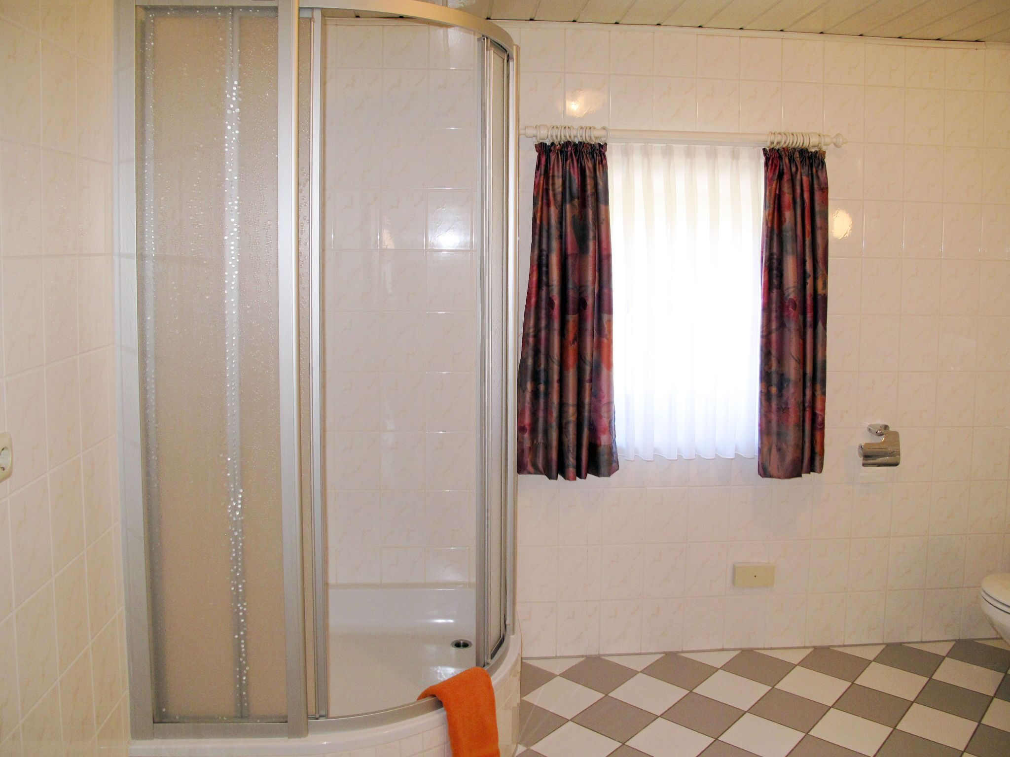 A bathroom with a shower enclosure, a window with curtains, and a checkered floor.