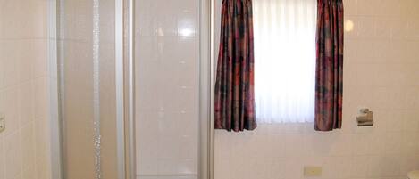 A bathroom with a shower enclosure, a window with curtains, and a checkered floor.
