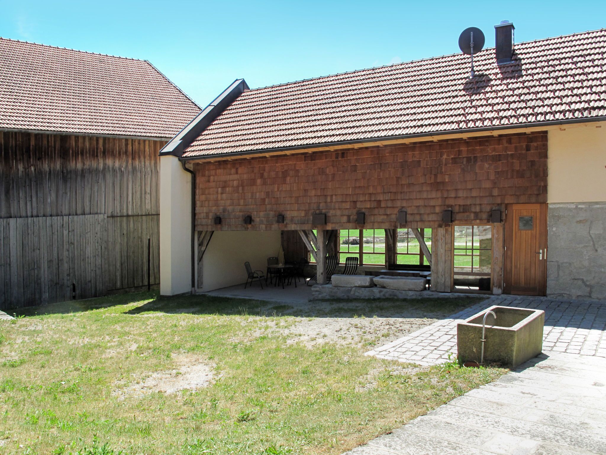A building with a tiled roof, a wooden door, and a brick patio area with outdoor seating.