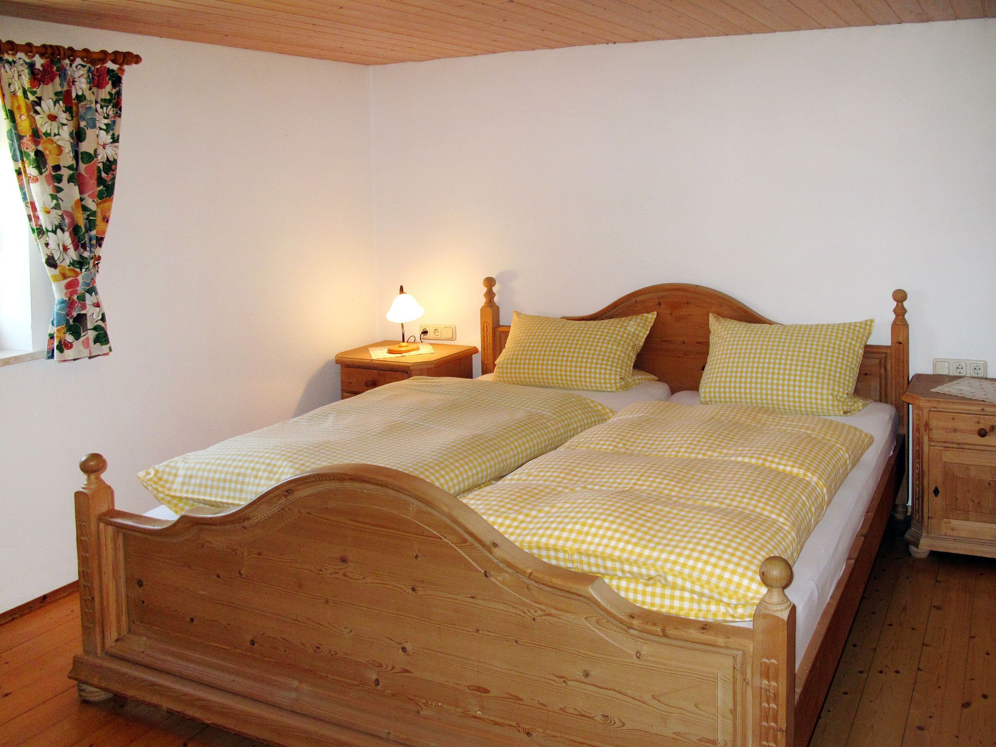 Un lit double avec une tête de lit en bois, deux tables de chevet avec des lampes et une fenêtre agrémentée de rideaux à motifs floraux.