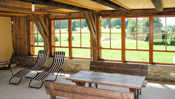 Una habitación rústica de madera con un gran ventanal, dos sillones a rayas y una mesa de madera.