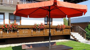 A wooden bench and picnic table under a red umbrella, with flower baskets on a balcony. - Hagengruber by Interhome (Bischofsmais)