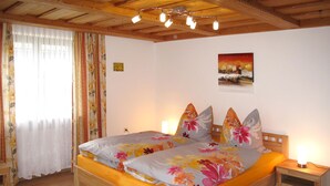 A wooden-framed bed with floral bedding, a nightstand with a lamp, and a painting on the wall. - Hagengruber by Interhome (Bischofsmais)