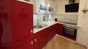 A modern kitchen with red cabinets, stainless steel appliances, and a built-in oven. - Kühbeck by Interhome (Bischofsmais)