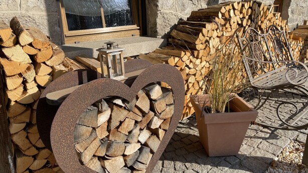 A rustic outdoor seating area with a heart-shaped firewood stack, a lantern, and a metal bench. - Kühbeck by Interhome (Bischofsmais)