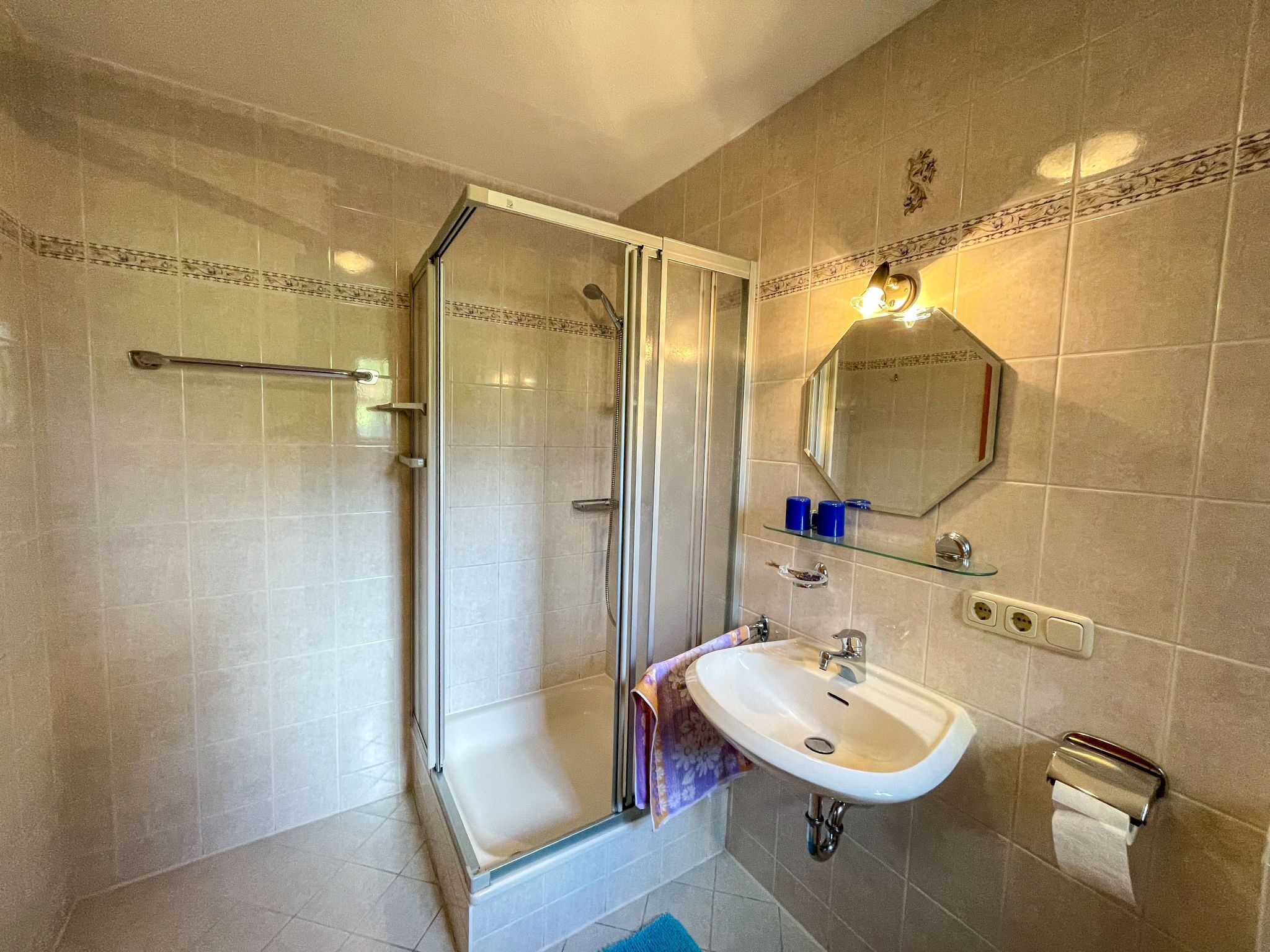 Un baño con cabina de ducha de vidrio, un lavabo con espejo y un perchero para toallas.