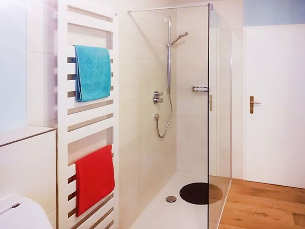 Une salle de bain moderne avec une douche à parois de verre, des murs recouverts de carreaux blancs et un plancher en bois.