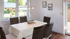 Un comedor con una mesa dispuesta para seis personas, rodeada de sillas de mimbre, un mantel blanco y una lámpara colgante.