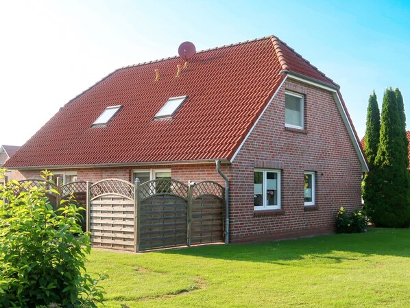 A two-story house with a red-tiled roof, a brick exterior, and a fenced yard.