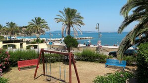 A beach view with a swing set, a blue bench, and a sandy area with palm trees.