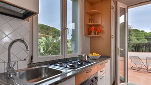 A modern kitchen with a stainless steel sink, granite countertop, and a gas stove. There is a window with a view of greenery outside.