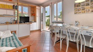 A compact kitchen with a TV, a dining area with a table and chairs, and a bed with a checkered blanket.