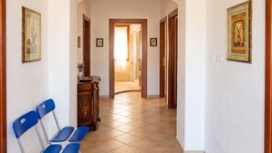 Un passadís amb cadires blaves, un armari de fusta i quadres amb marc a les parets.