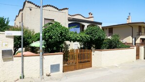 Una casa de dues plantes amb teulada de rajola, una porta de fusta i un cartell que diu "GRECIA".