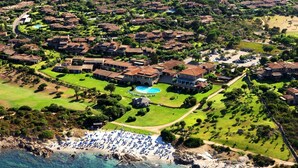 Vista aérea de un complejo turístico frente al mar con villas, piscina y zona de playa.