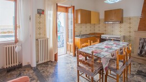 A compact kitchen with wooden cabinets, a dining table with a patterned tablecloth, and a view of the outside balcony. - Villa Teresa by Interhome (Peschici)