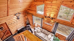 A cozy cabin interior with a wooden interior, a sofa, a table, and large windows offering views of the outdoors.