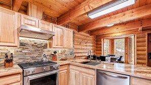 A log cabin kitchen with wooden cabinets, a stone backsplash, a gas stove, and a dishwasher.